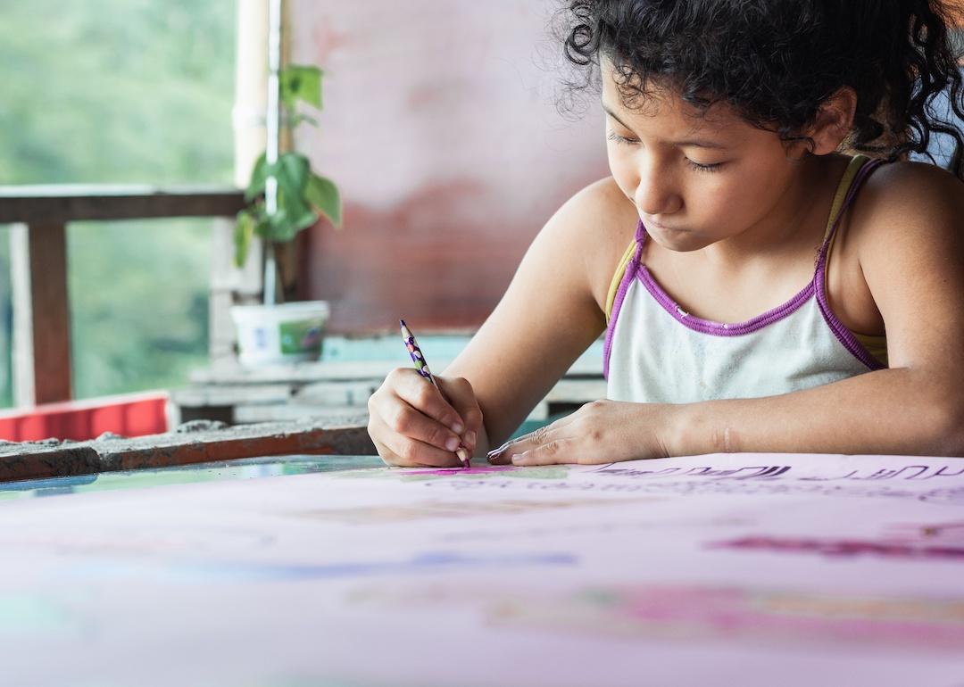Closeup of a little girl coloring with a purple pencil.