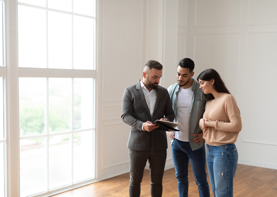 A young couple stands in an empty house talking to a realtor.