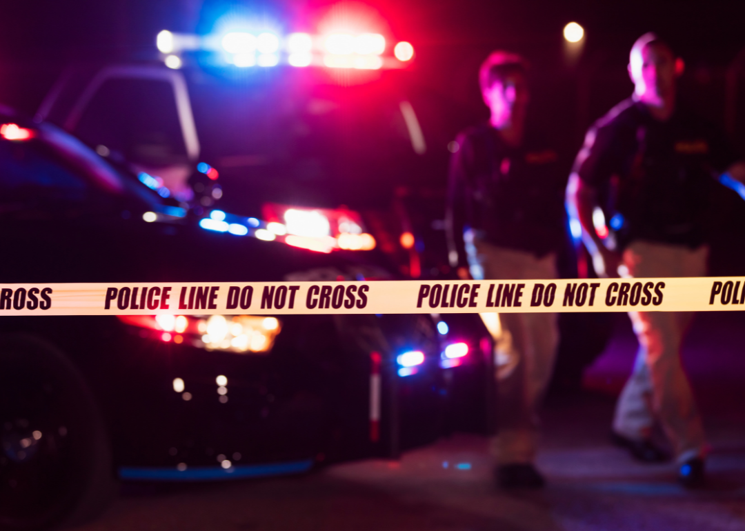 Crime scene tape, yellow, with blurred image of police officers in background