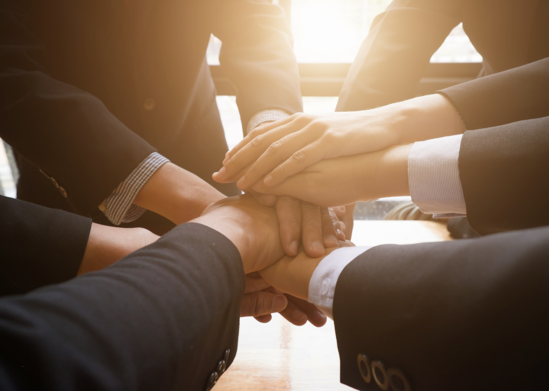 A group of suited individuals stands in a circle and places their hands in the middle of the group