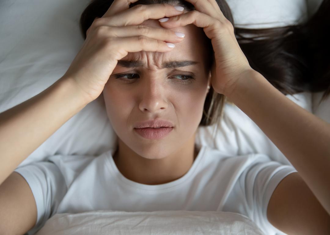 A person in bed holding their head after being awoken by a hypnic jerk.