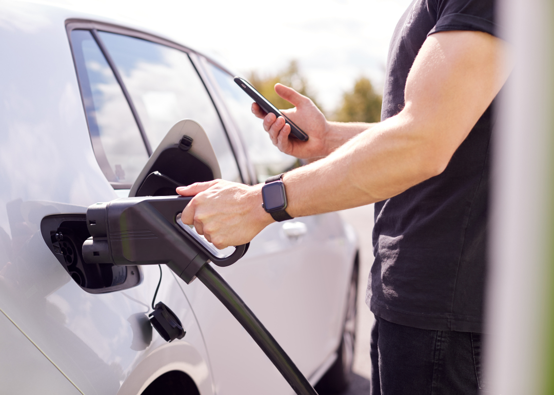 A man charges an electric vehicle while looking at his smartphone
