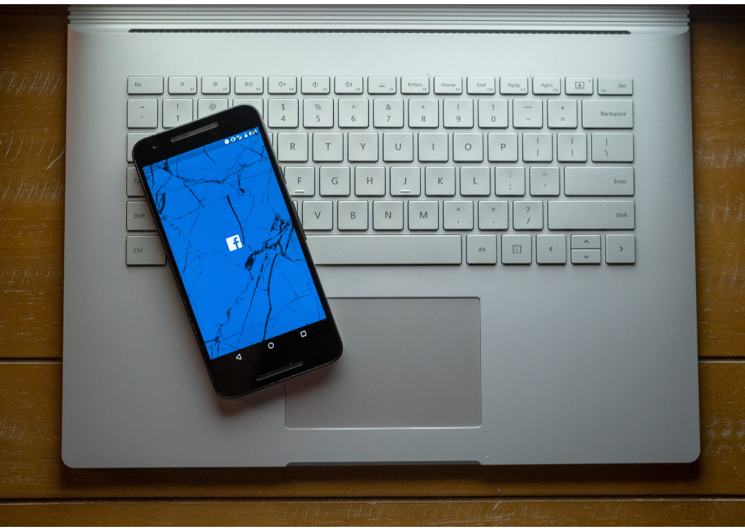 A cracked phone with the Facebook app loading sitting on a laptop.