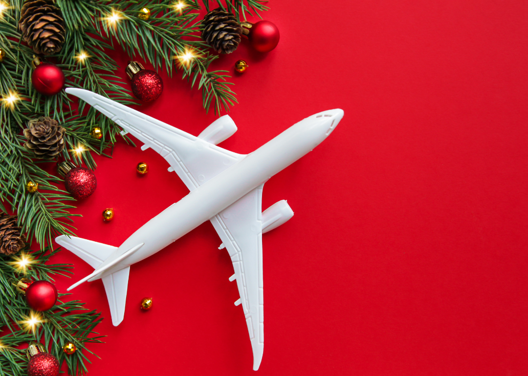 A conceptual image of a white airplane model against a red background with holiday foliage