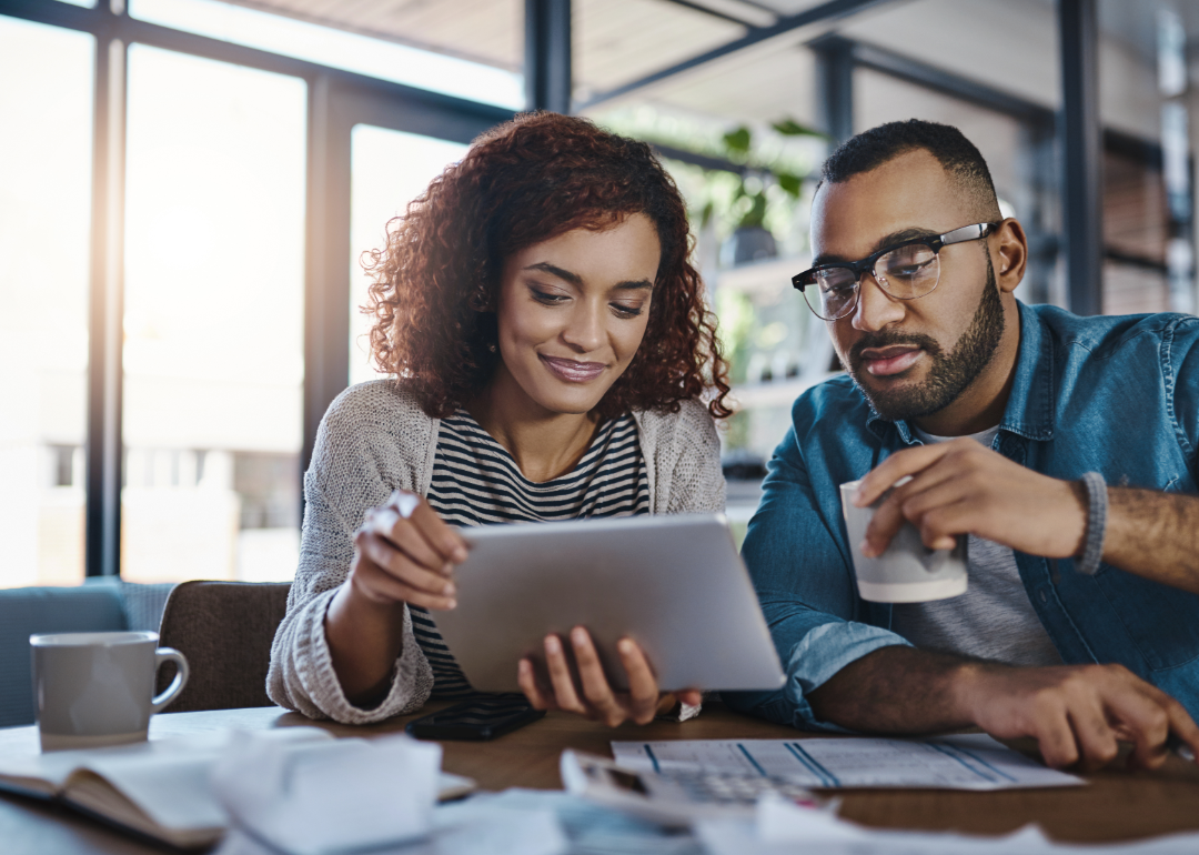 a man and woman at a table look over documents and tablet 