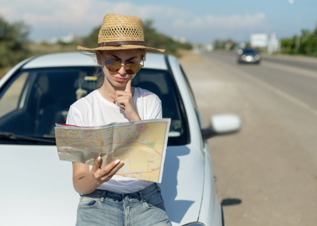 A woman reads a roadmap by the side of the road.