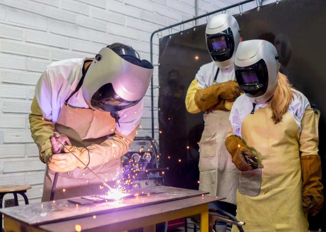 two college-age students watching their classmate practice welding
