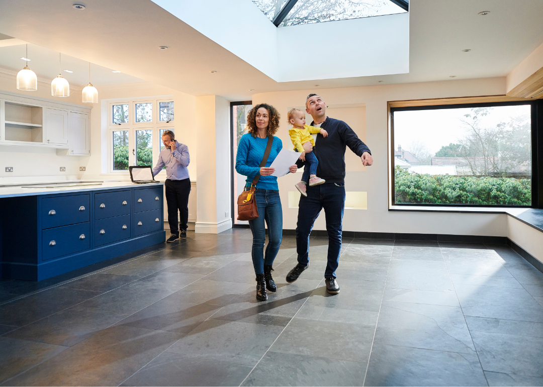 couple with young child views open house with realtor in the background