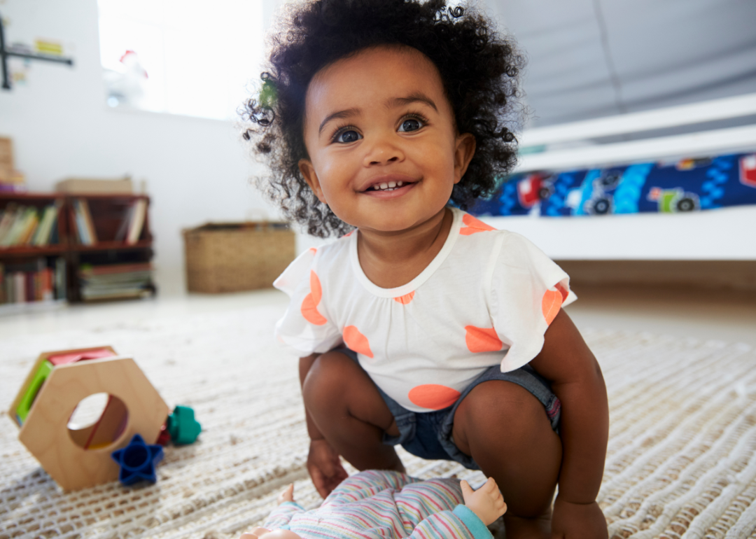 A happy baby wearing a polka dots plays with a baby doll.