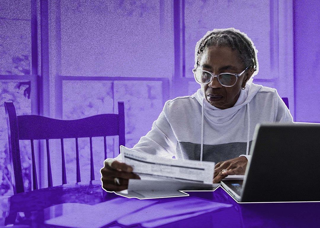 woman looks over bills while background has been shaded purple for dramatic effect