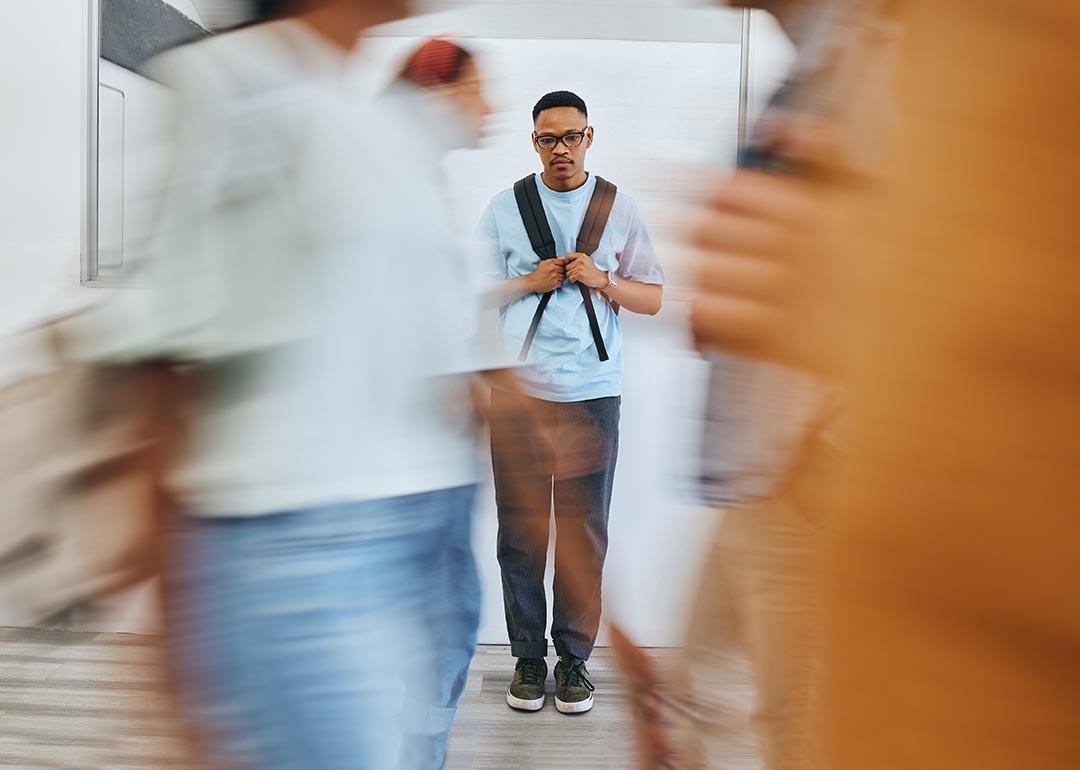serious young man standing in school hallway with backpack with motion blur of students passing in front