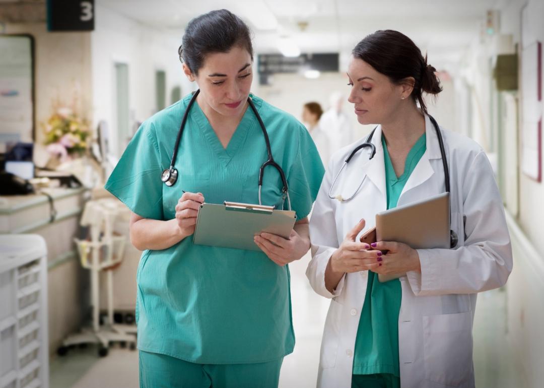 Nurse walking with a doctor discussing paperwork.