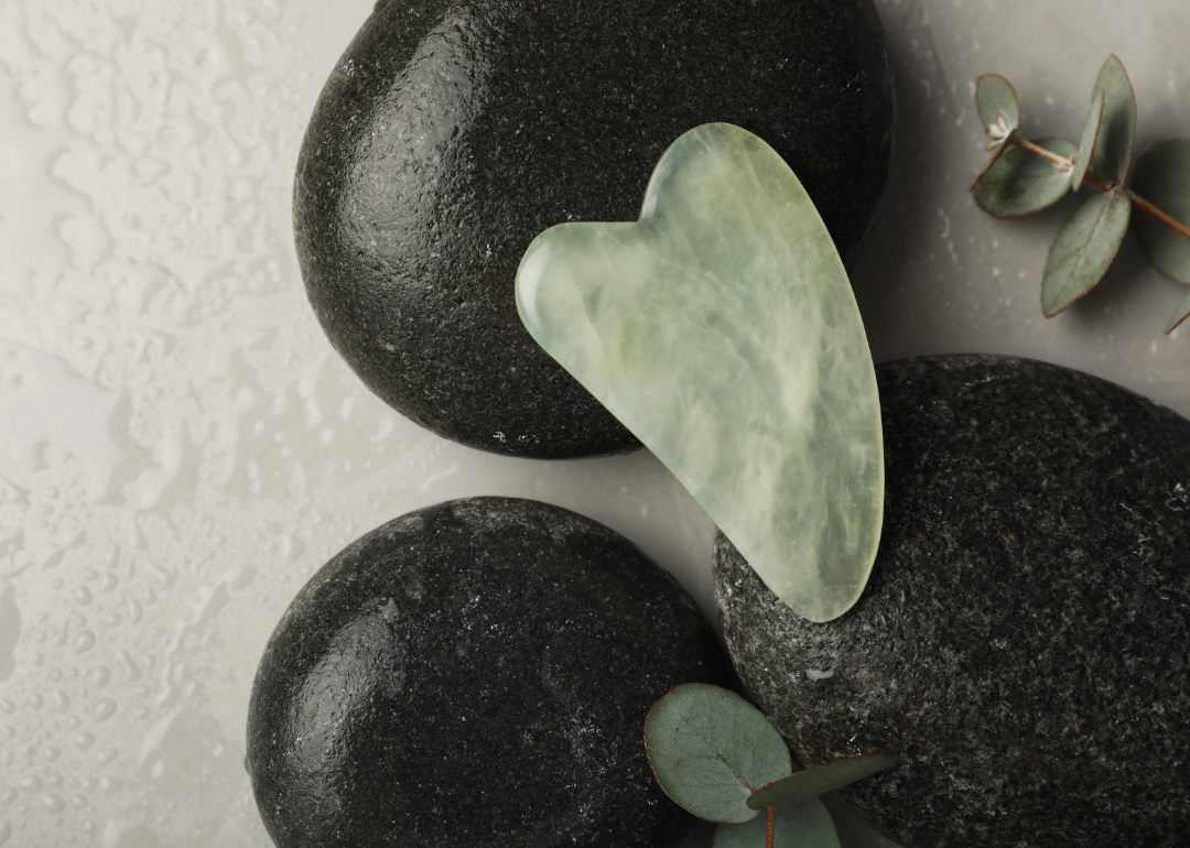 jade color gua sha tool displayed on black stones