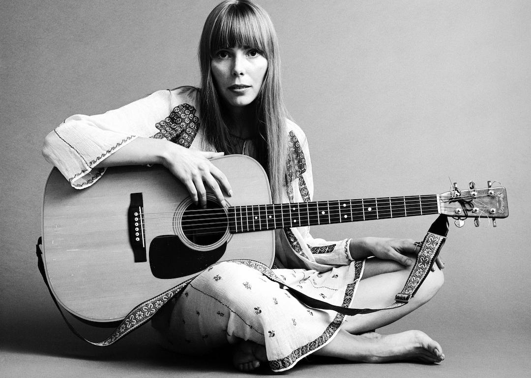 Portrait of musician Joni Mitchell seated on the floor with her acoustic guitar in her lap in 1968.
