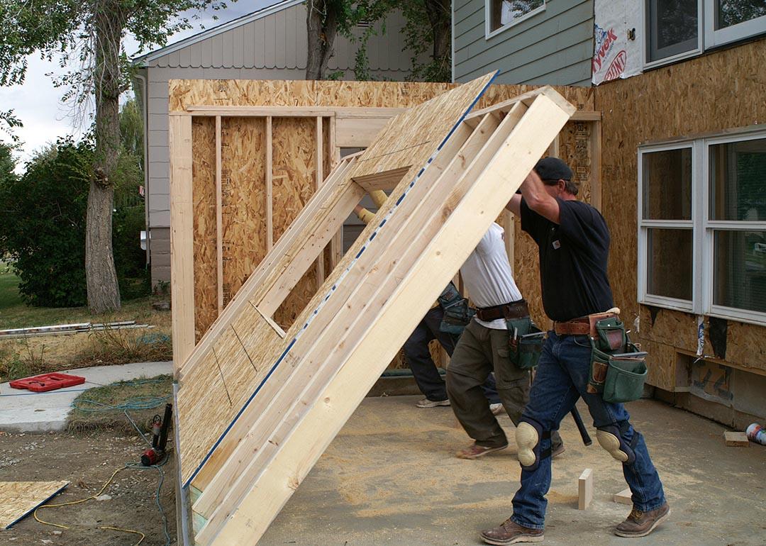 two people raising the plywood frame where a wall will go up during a home addition