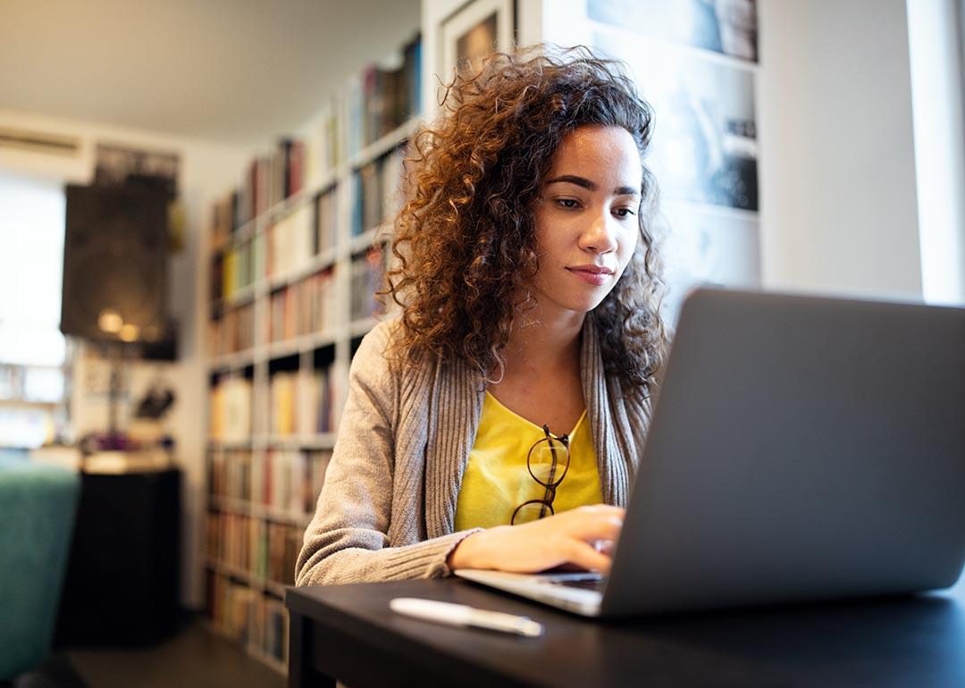 Young adult working on laptop with books on bookshelf in background.