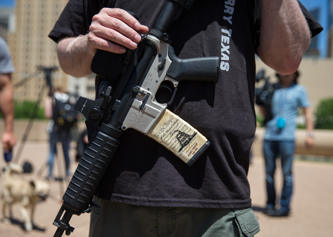 Person with an assault rifle across their chest, a miniature copy of the American constitution on the gun handle, at a counter-protest by gun advocates in response to protesters opposing the NRA's annual convention in Dallas, Texas, 2018.