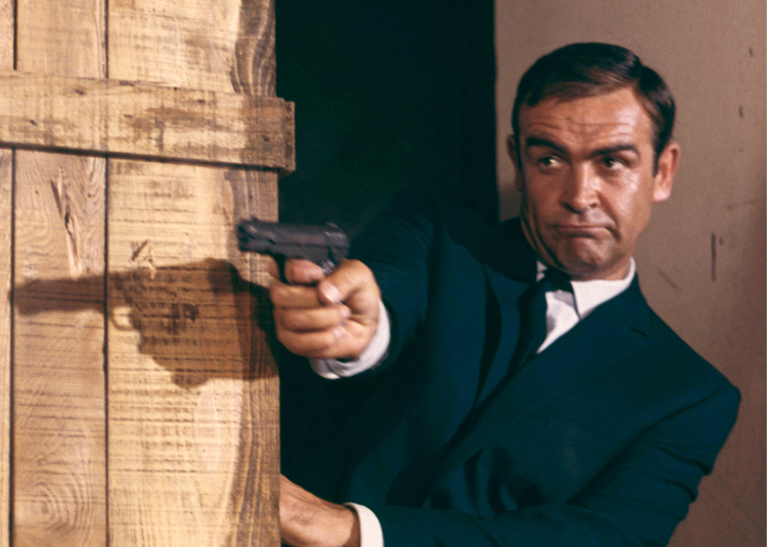 Sean Connery as James Bond 007 firing a pistol behind crates from the film "Goldfinger", 1964.