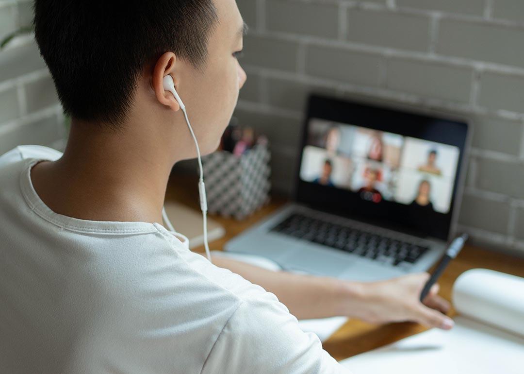 Young person with headphones works on computer with virtual meeting, in dorm setting.