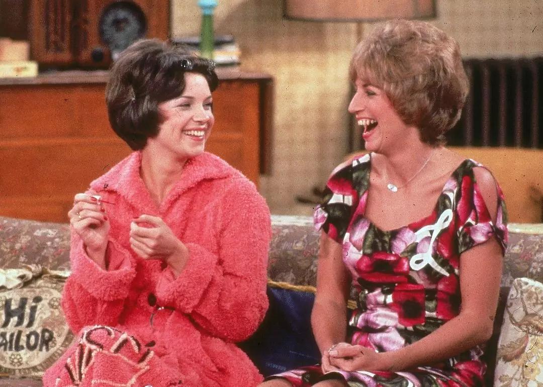 Actors Cindy Williams and Penny Marshall sit on their sofa laughing in a still from 'Laverne and Shirley.'