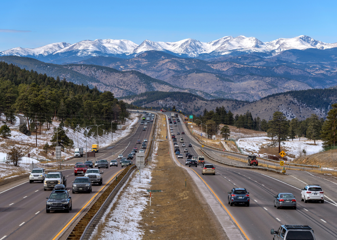 A sunny winter day view of busy Interstate Highway I-70, with snow-capped high peaks of the Continental Divide towering at west.