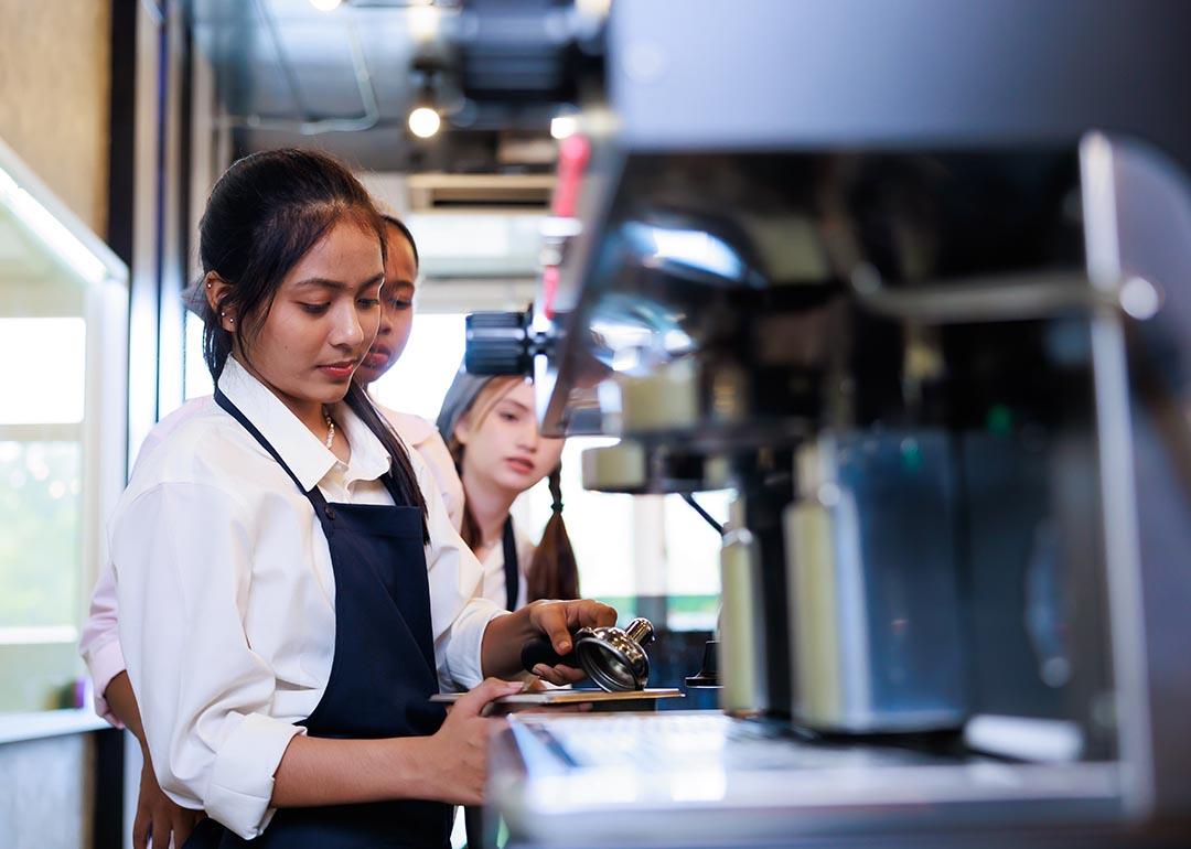 Three young workers in a coffee shop training to become baristas.