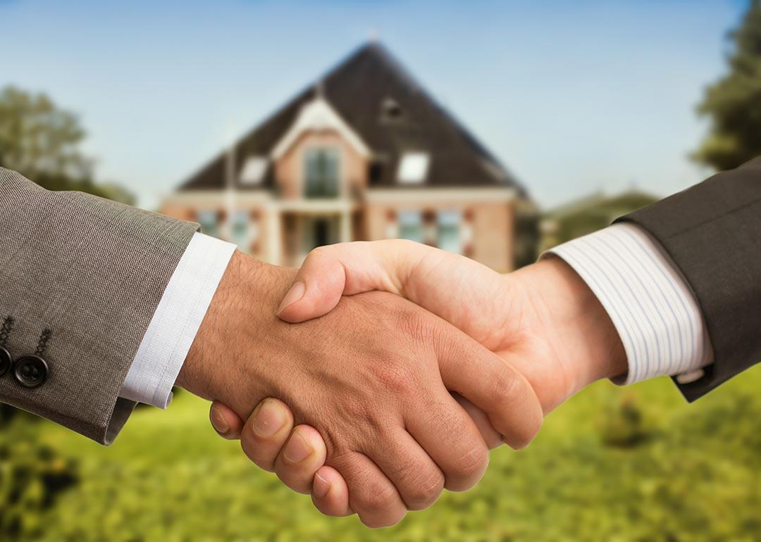 Handshake between two people with blurred house in background. 