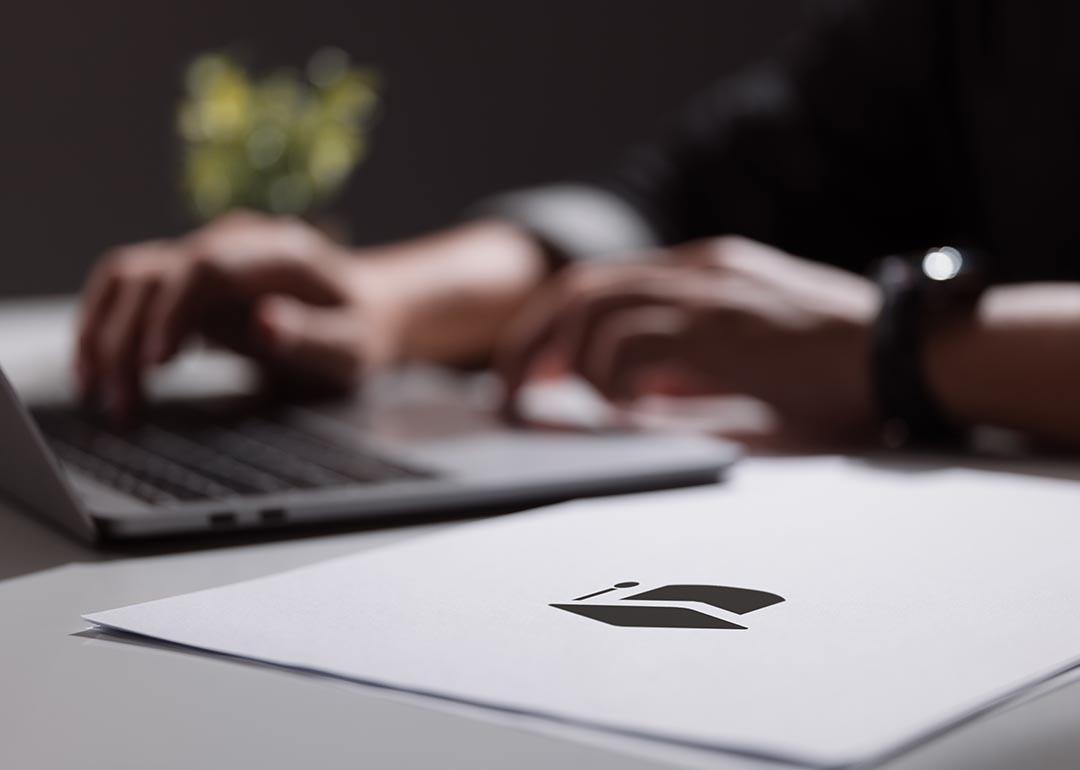 Person working on a laptop computer backlit with paperwork in the foreground.