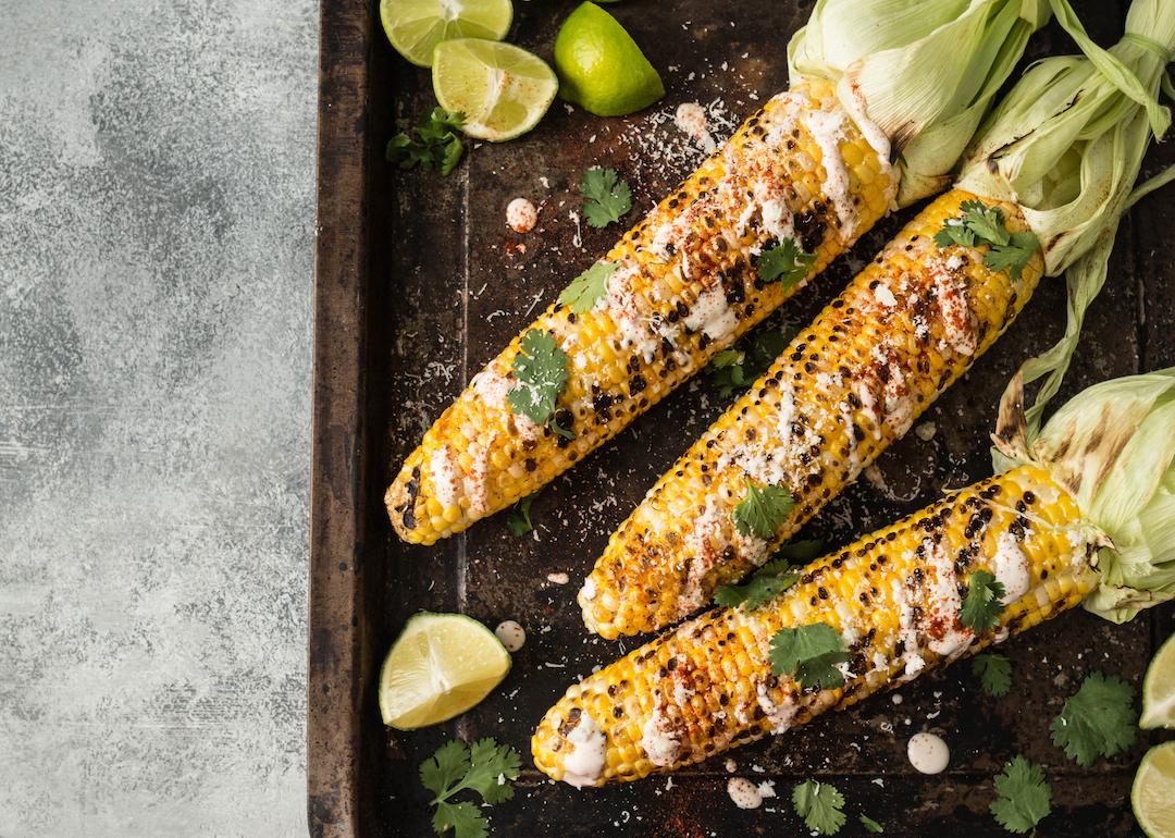Grilled corn cobs with sauce, coriander, lime, paprika, and cheese.