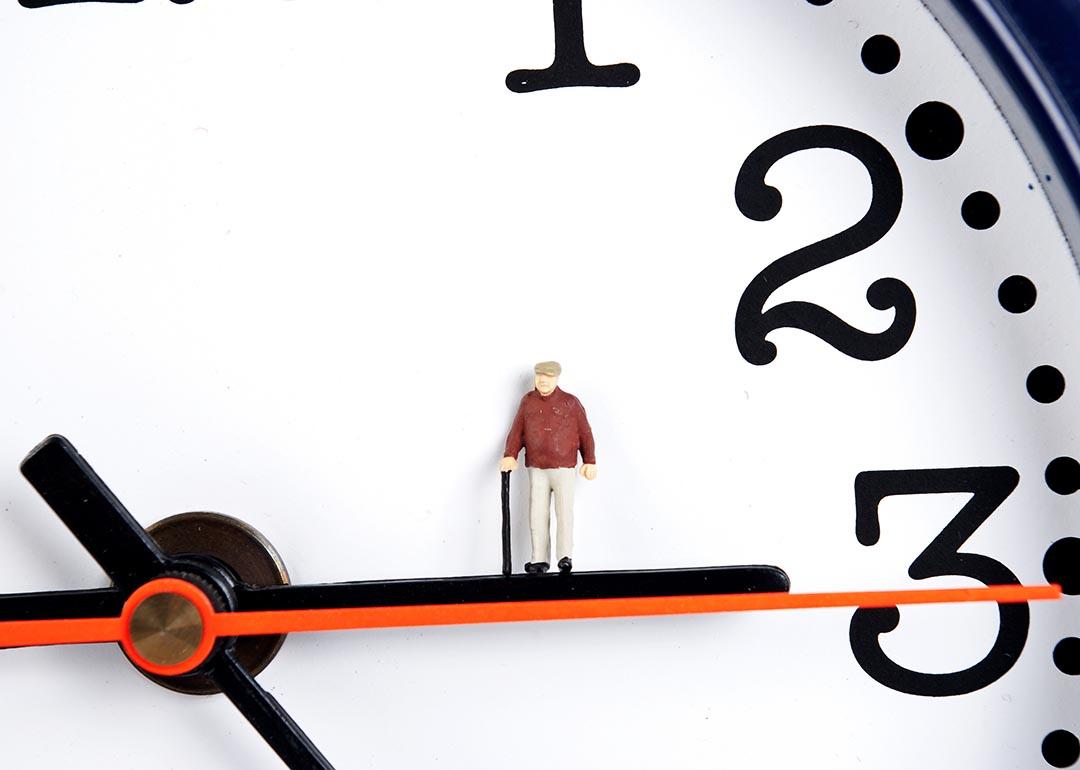 Concept of longevity illustrated by clock with miniature old man figurine place on the hour hand.