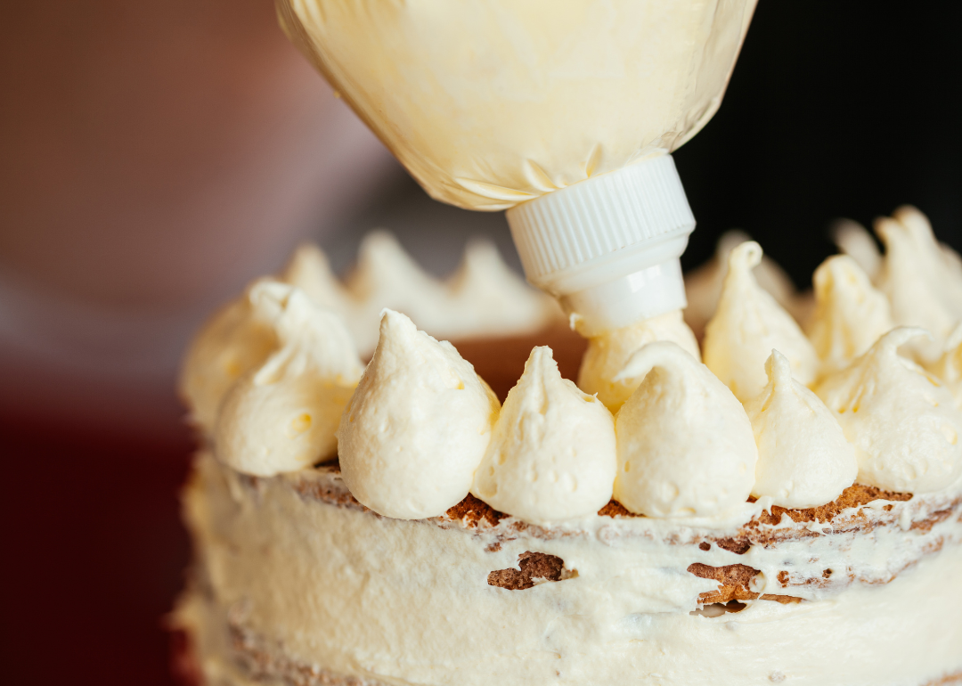 White icing being piped on a cake