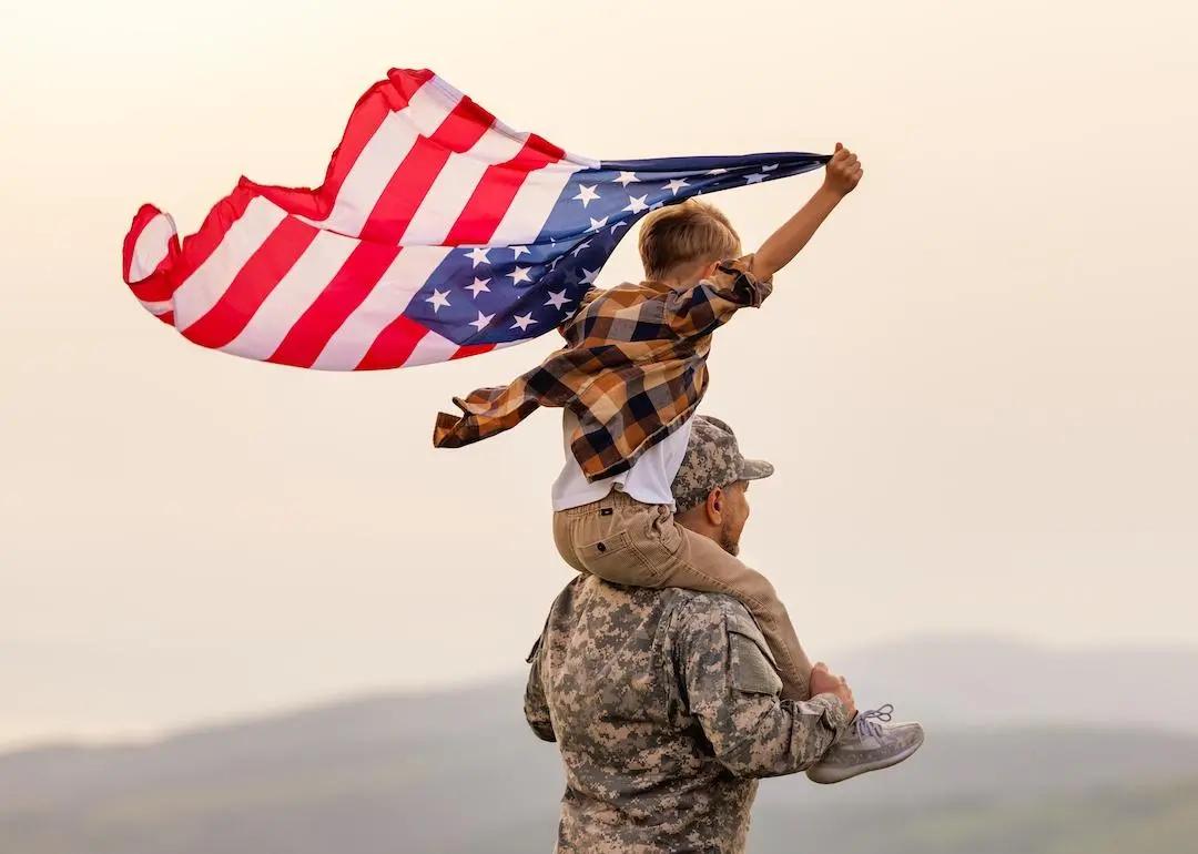 Military soldier carrying child with an American flag on shoulders.
