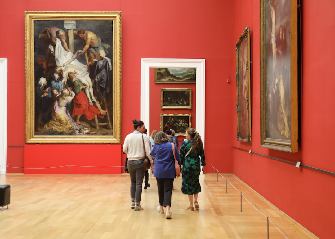 Museum visitors walk through an exhibition with art on red-orange walls inside Lille’s Palais des Beaux-Arts.