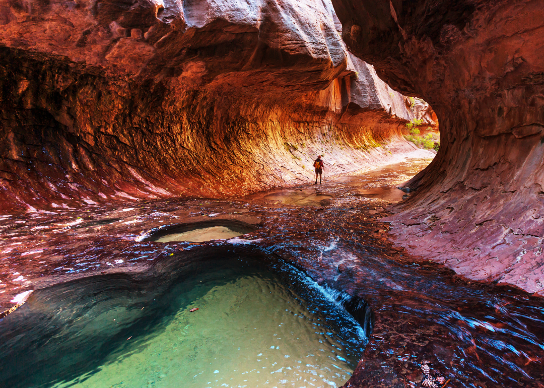 Hiker wading through the waters of the Narrows slot canyon in Zion National Park, Utah.