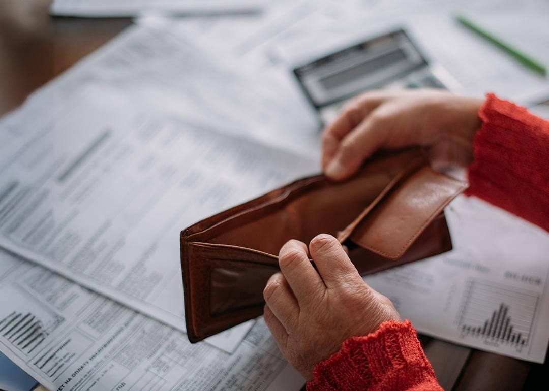 A woman's hands opening her empty wallet over a pile of power bills.
