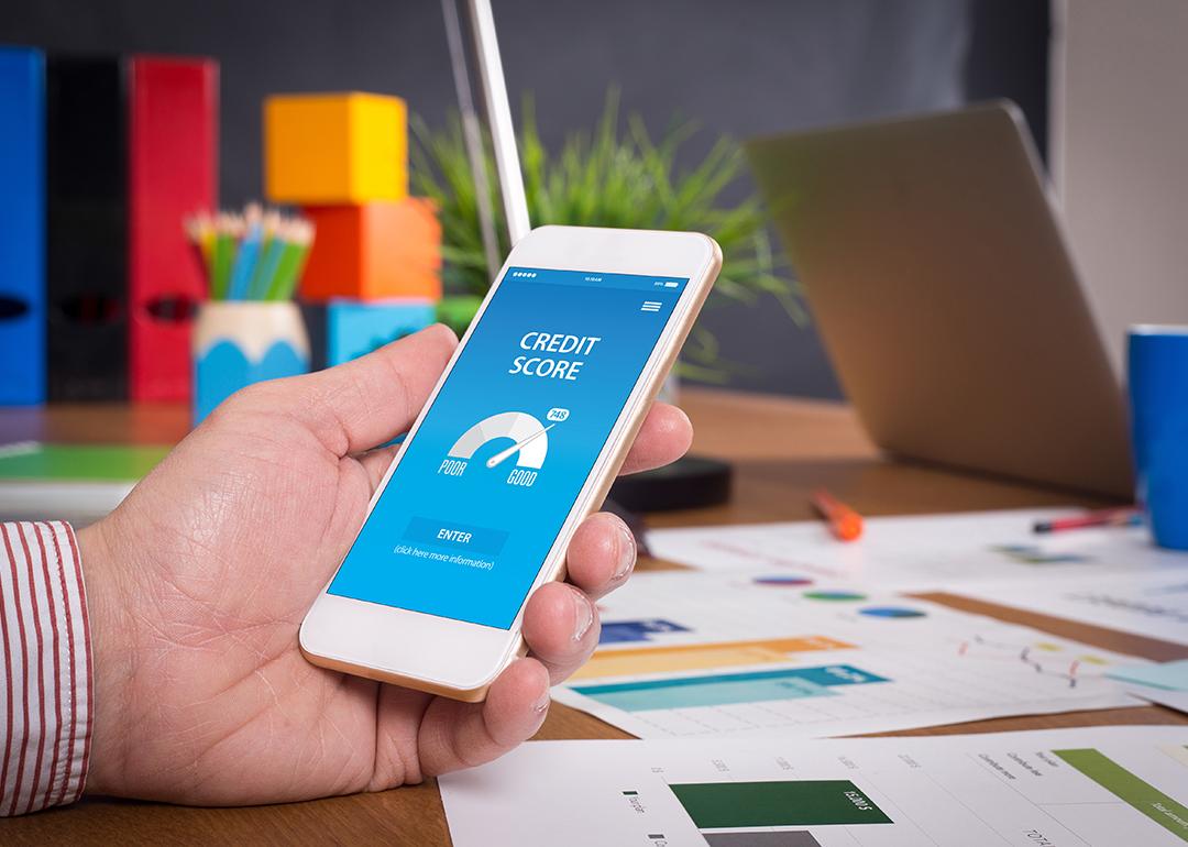 Employee in a workplace using a phone showing a credit score report.