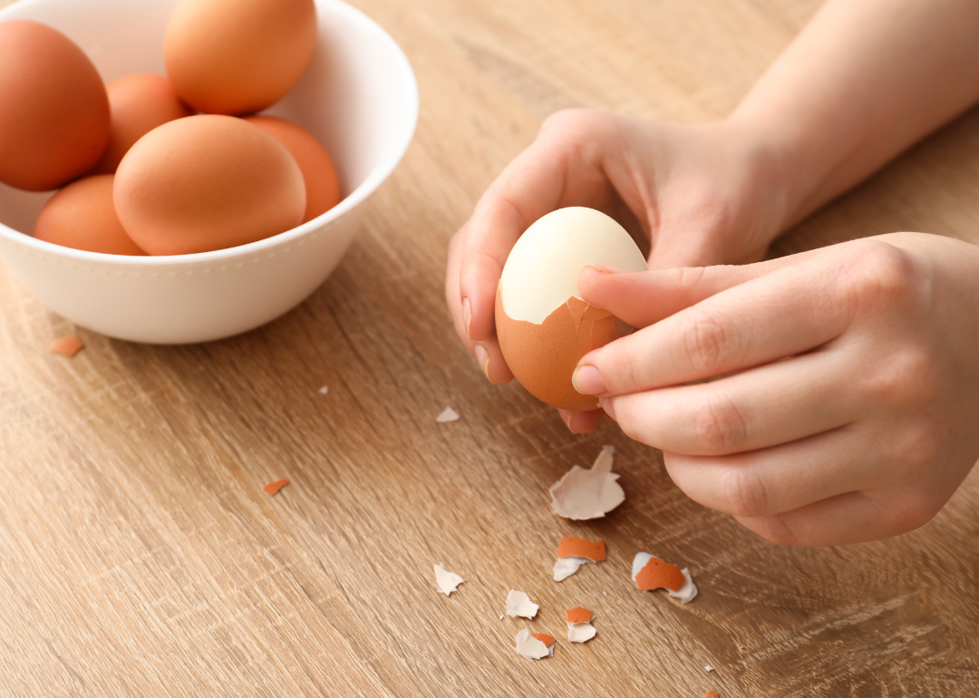 A person's hands peeling boiled eggs over a wooden countertop