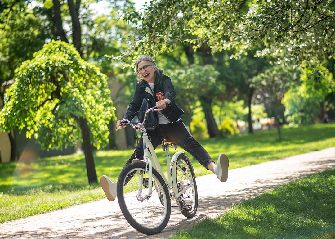 A middle aged woman happily having a stroll on a bike in a park.