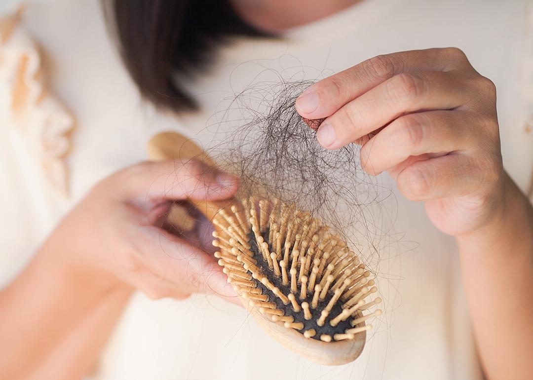A woman removing a thick tangle of hair from a hairbrush.