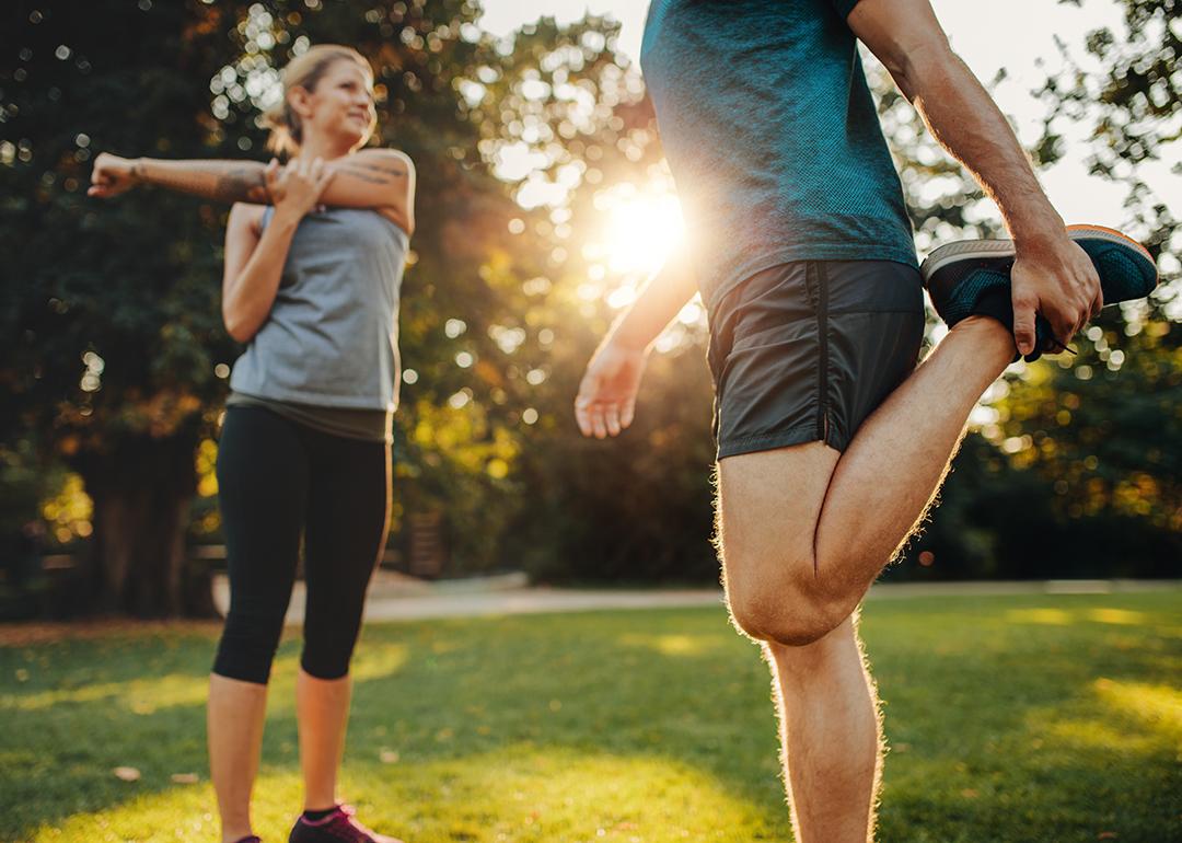 A man and a woman both stretching outdoors during a morning warmup.