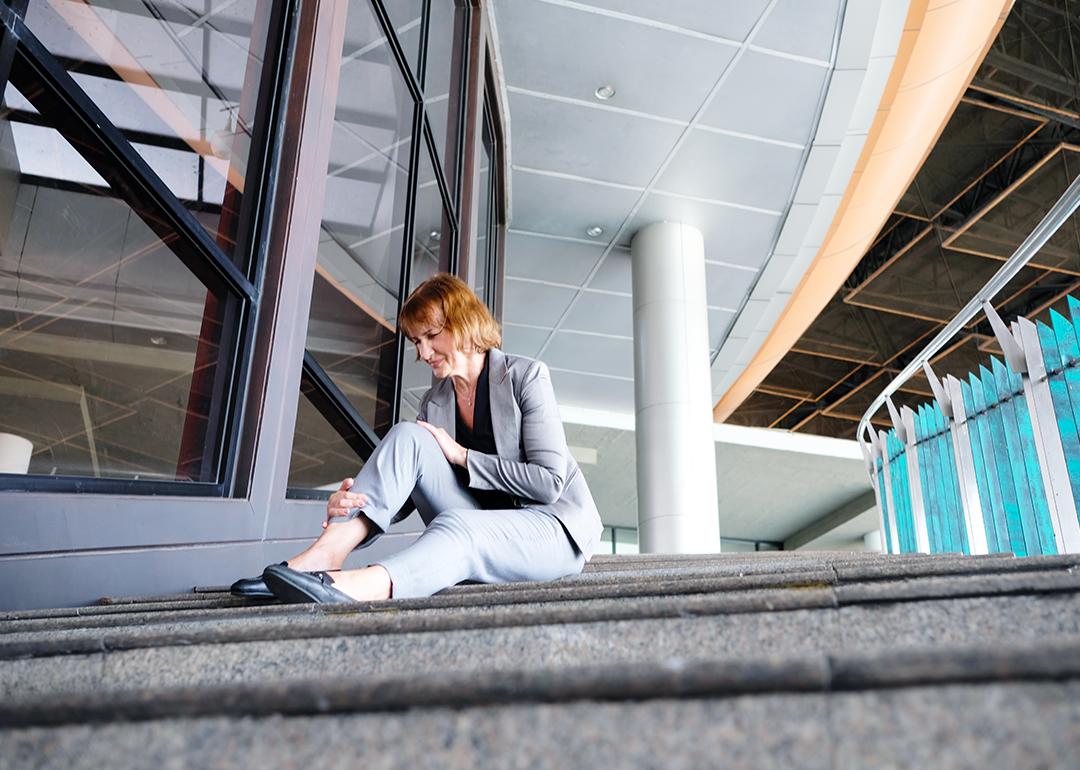 A woman at work sitting in pain after falling down the workplace stairs.