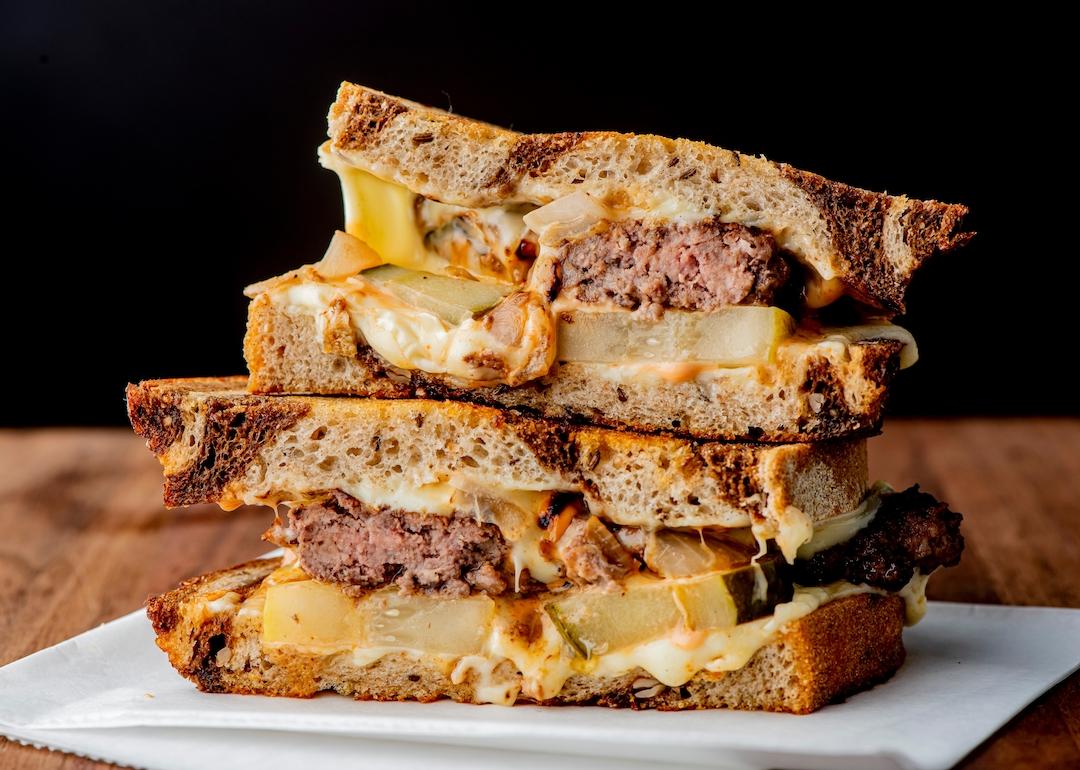 A patty melt consisting of a ground beef patty with melted cheese and topped with caramelized onions on two slices of griddled rye bread.