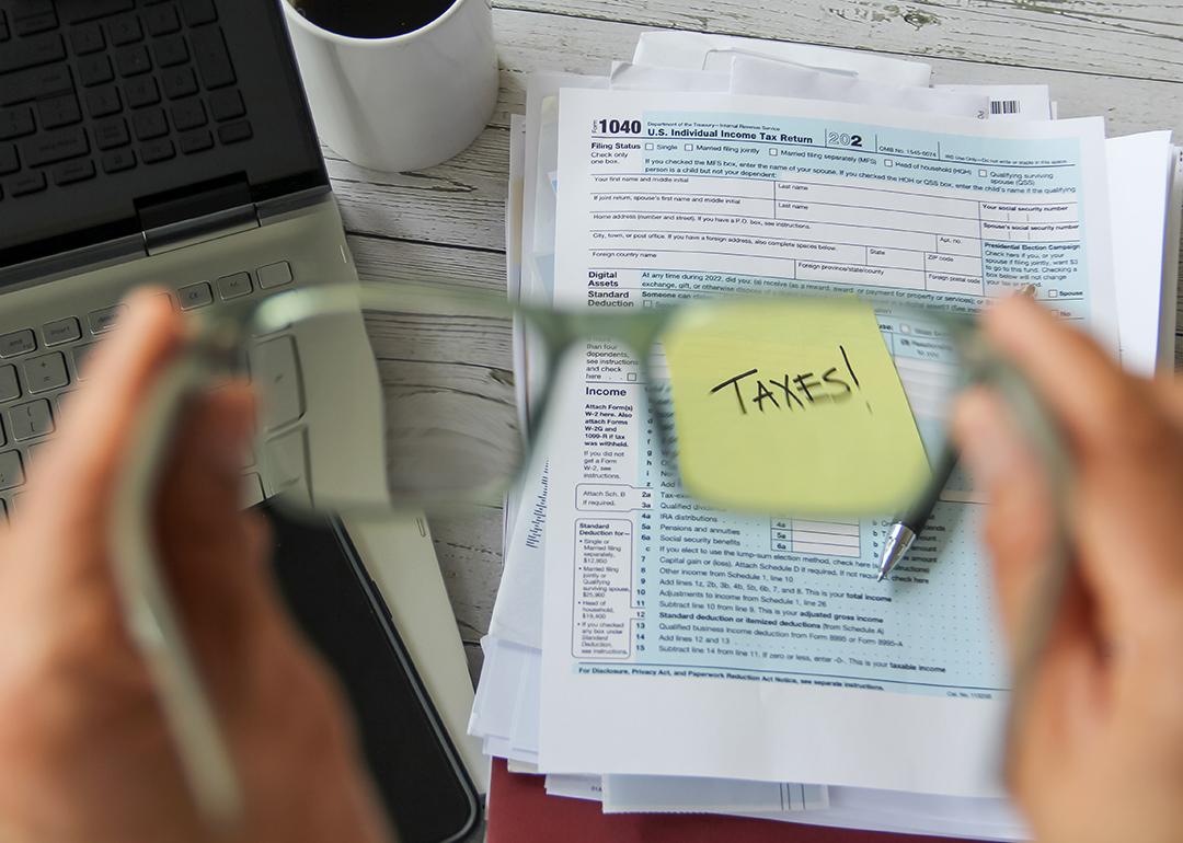 A selective focus of person holding eyeglasses over a tax form and the word "taxes" on a note.