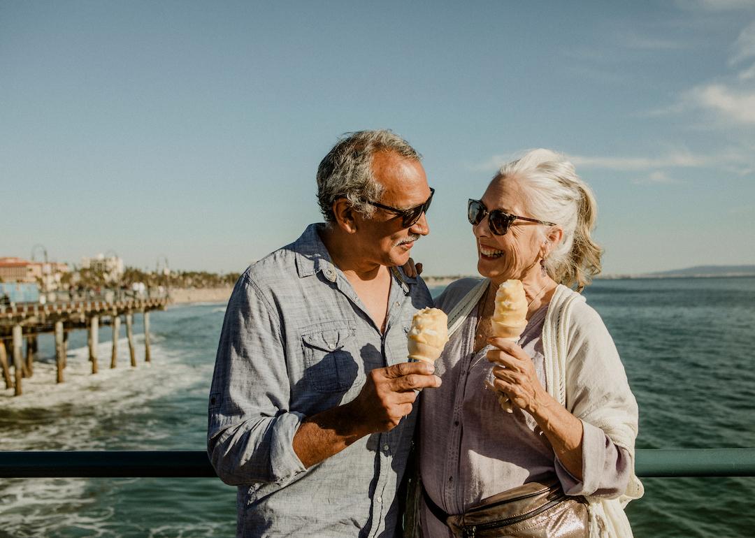 Smiling senior couple with ice cream cones standing near the beach in California.