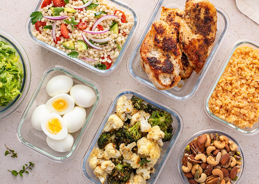 High protein meals such as roasted chicken breast, boiled eggs, various nuts and vegetables in meal prep containers.