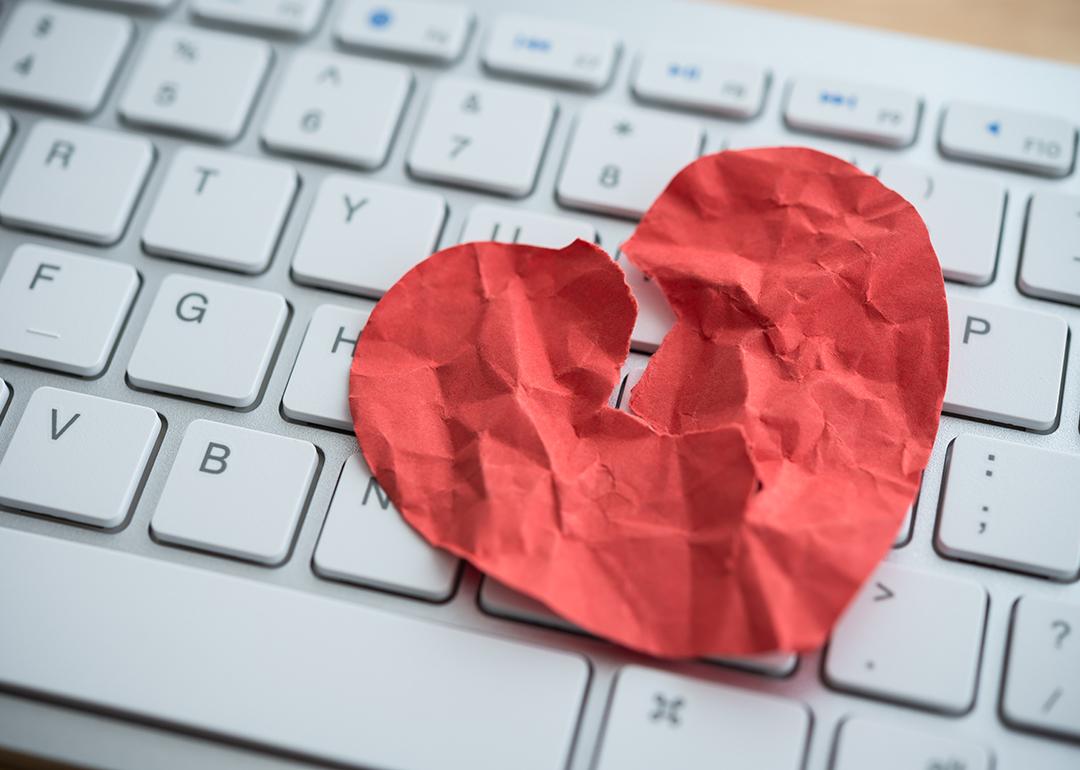 A red broken heart made out of paper on top of a computer keyboard depicting online dating scams.
