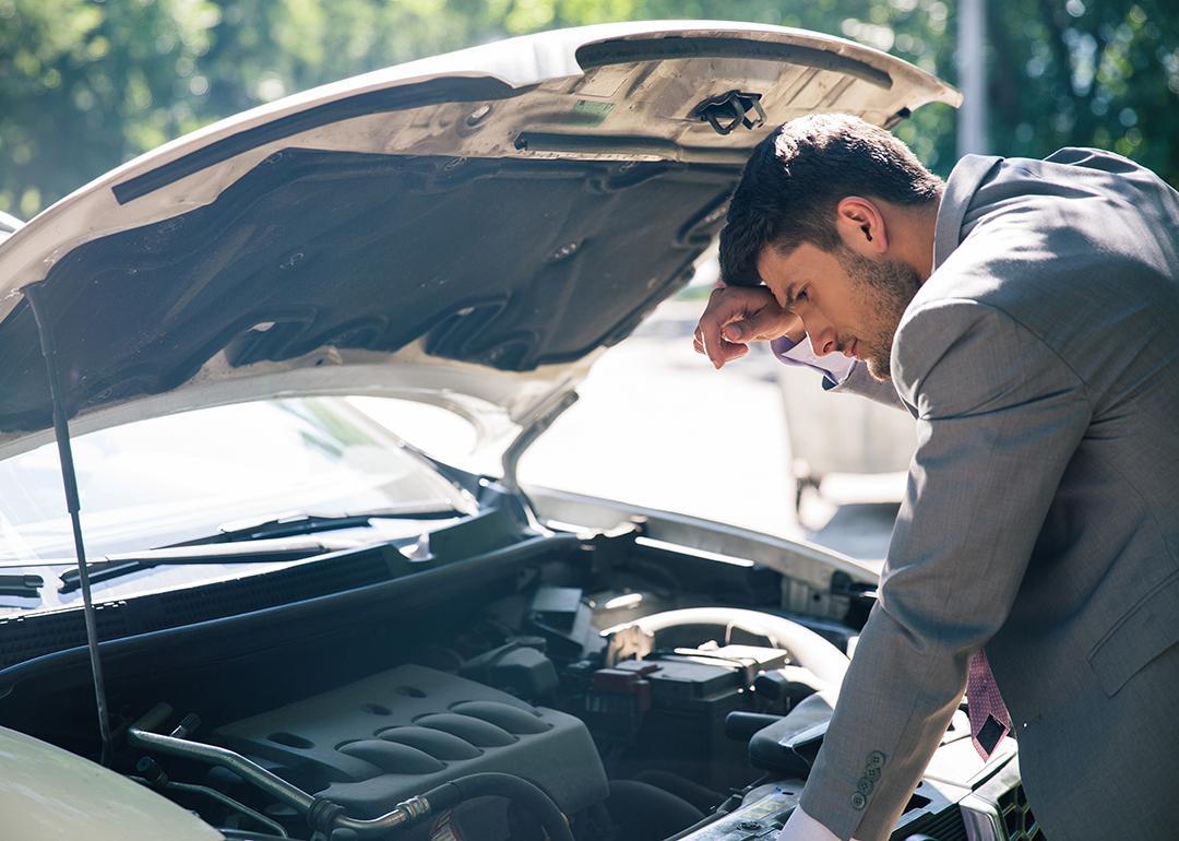A car owner inspects his car's hood after it breaks down.