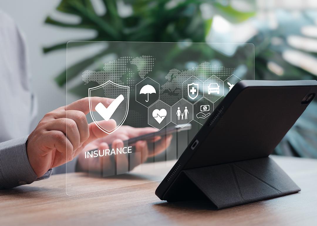Business professional using a work table and holographic icons of standard employee insurance concepts are shown.