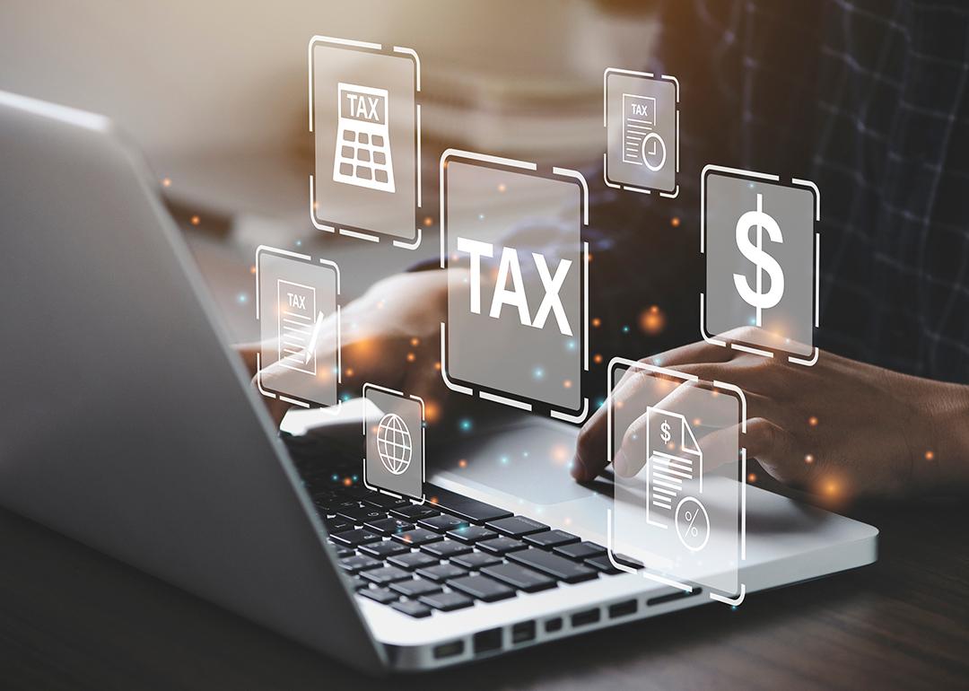 Businessperson using a laptop and holographic concepts of tax are illustrated.