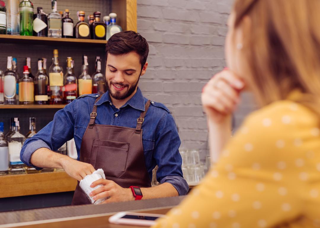 Bartender kindly smiling at customer while making a drink.